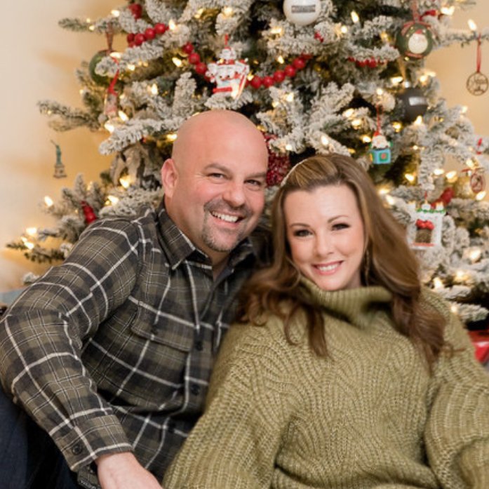 Santa Ink founders Sarah and Wayne smiling in front of a decorated Christmas tree